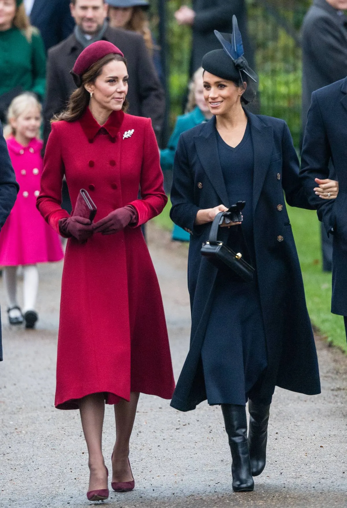 Meghan Markle wears a beret with navy feathers while walking next to Kate Middleton.