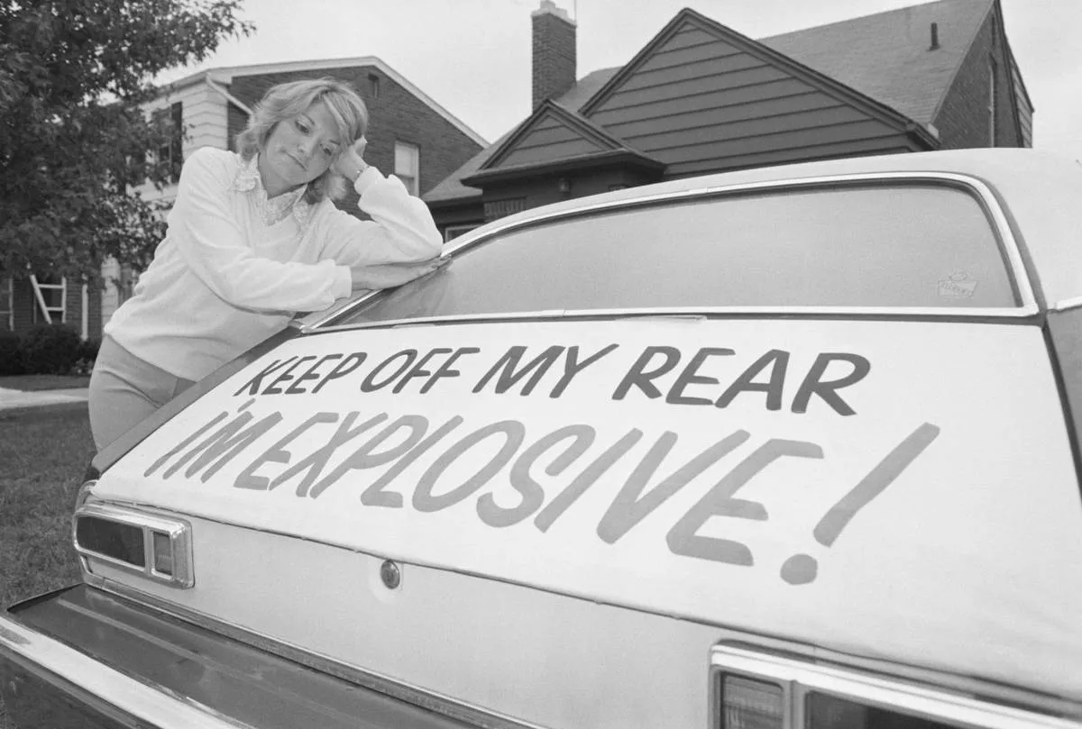 A woman leans on her Ford Pinto with a sign that says, 