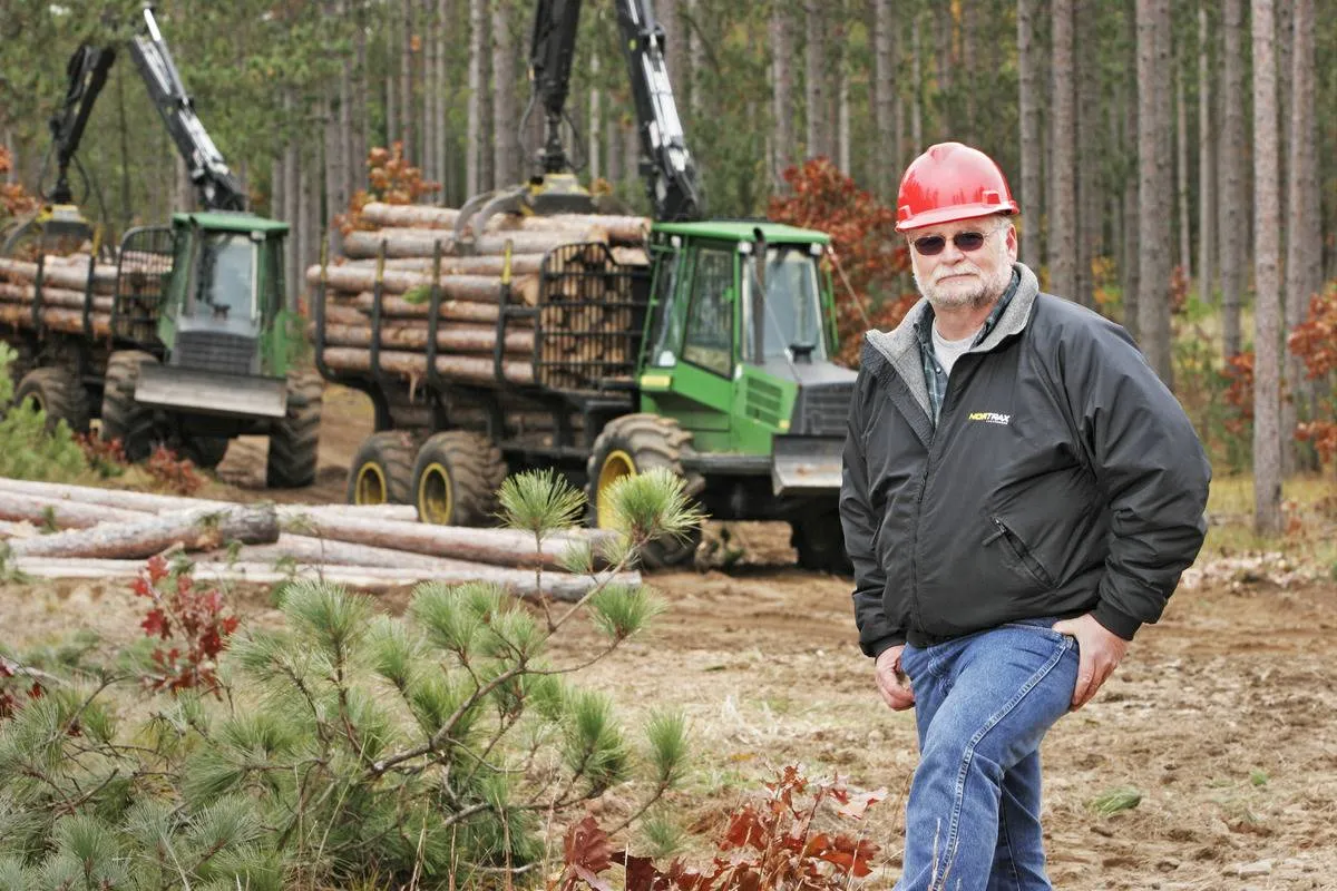 An employee stand in front of a timber harvesting truck.