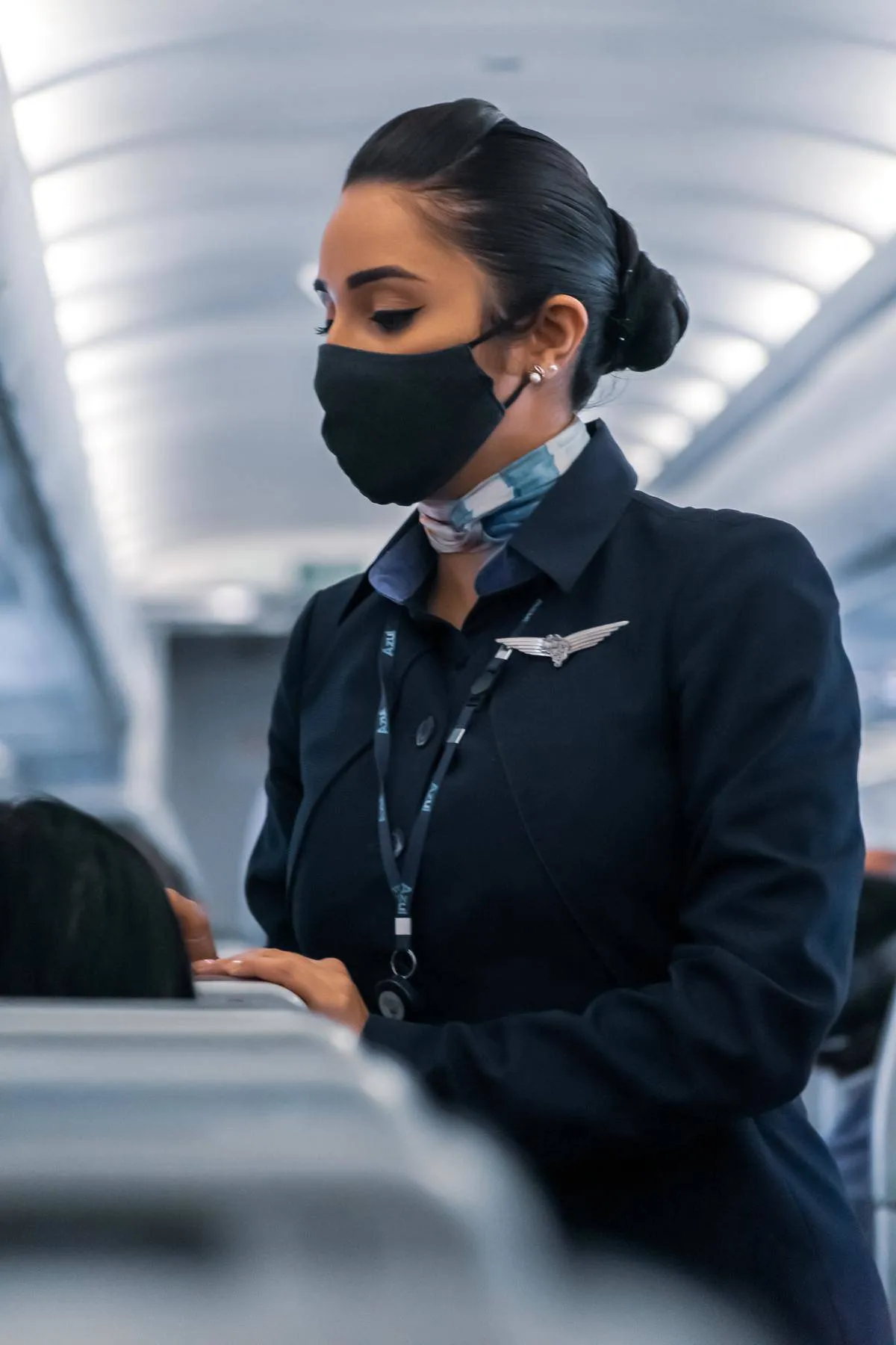 flight attendant with mask looking down towards passenger