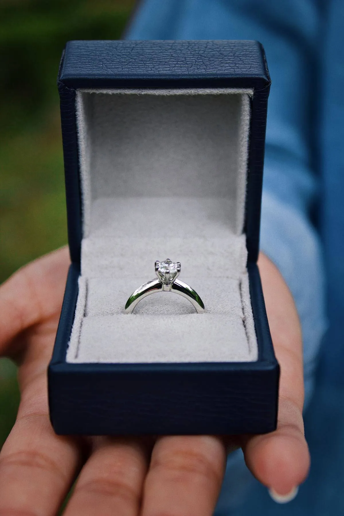 Hand holds out a box that contains a diamond engagement ring