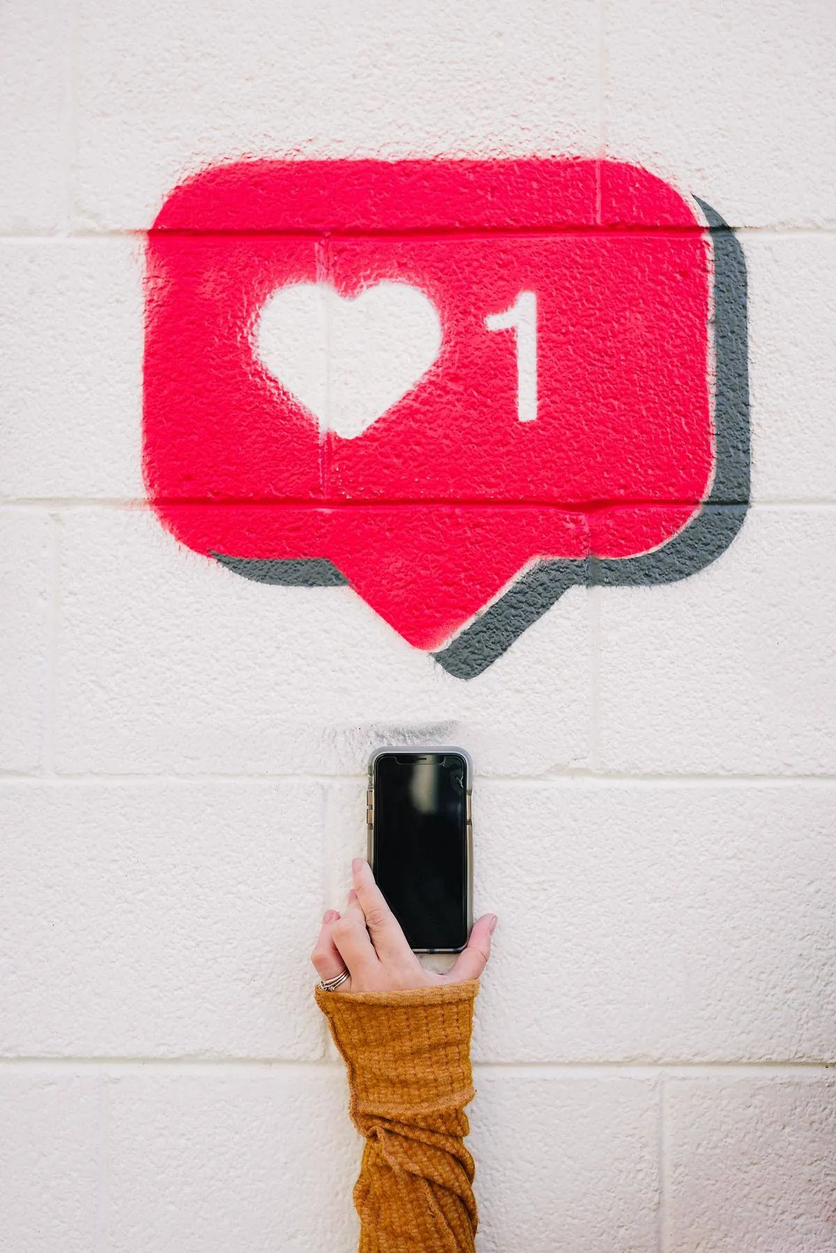 Woman holding a phone with Instagram notification painted on the wall behind her 