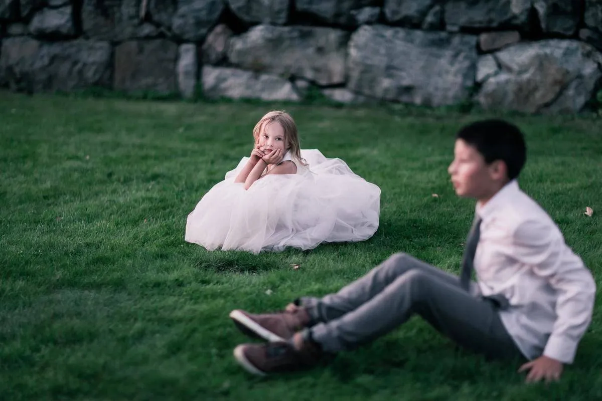 Flower girl and ring bearer sit on the grass