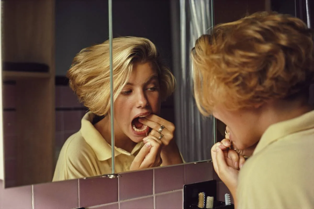 A woman flosses her teeth while looking into a mirror.
