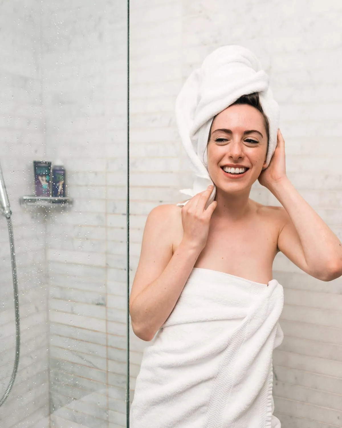 A woman with a towel wrapped around her hair exits the shower.