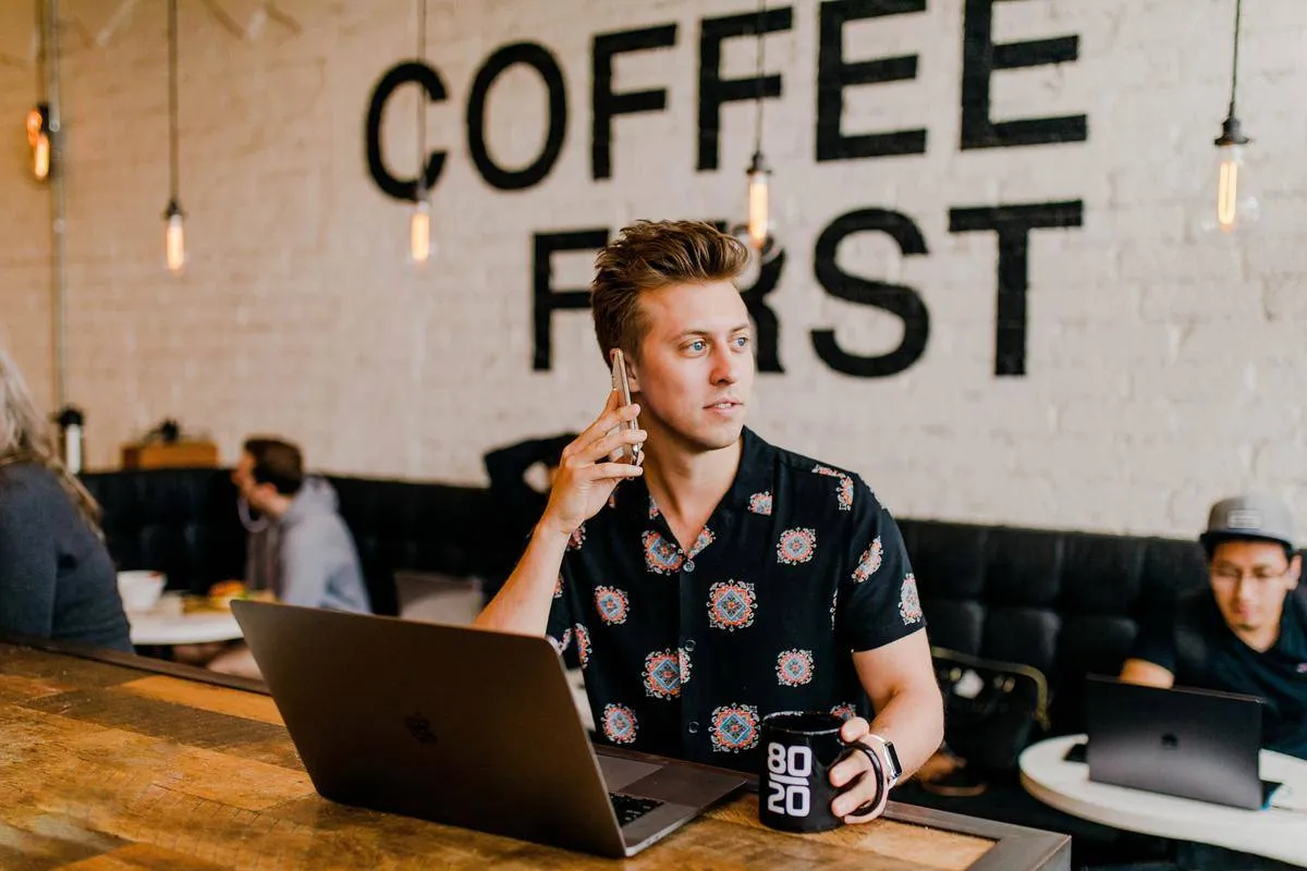 Man sits on cell phone at computer in coffee shop