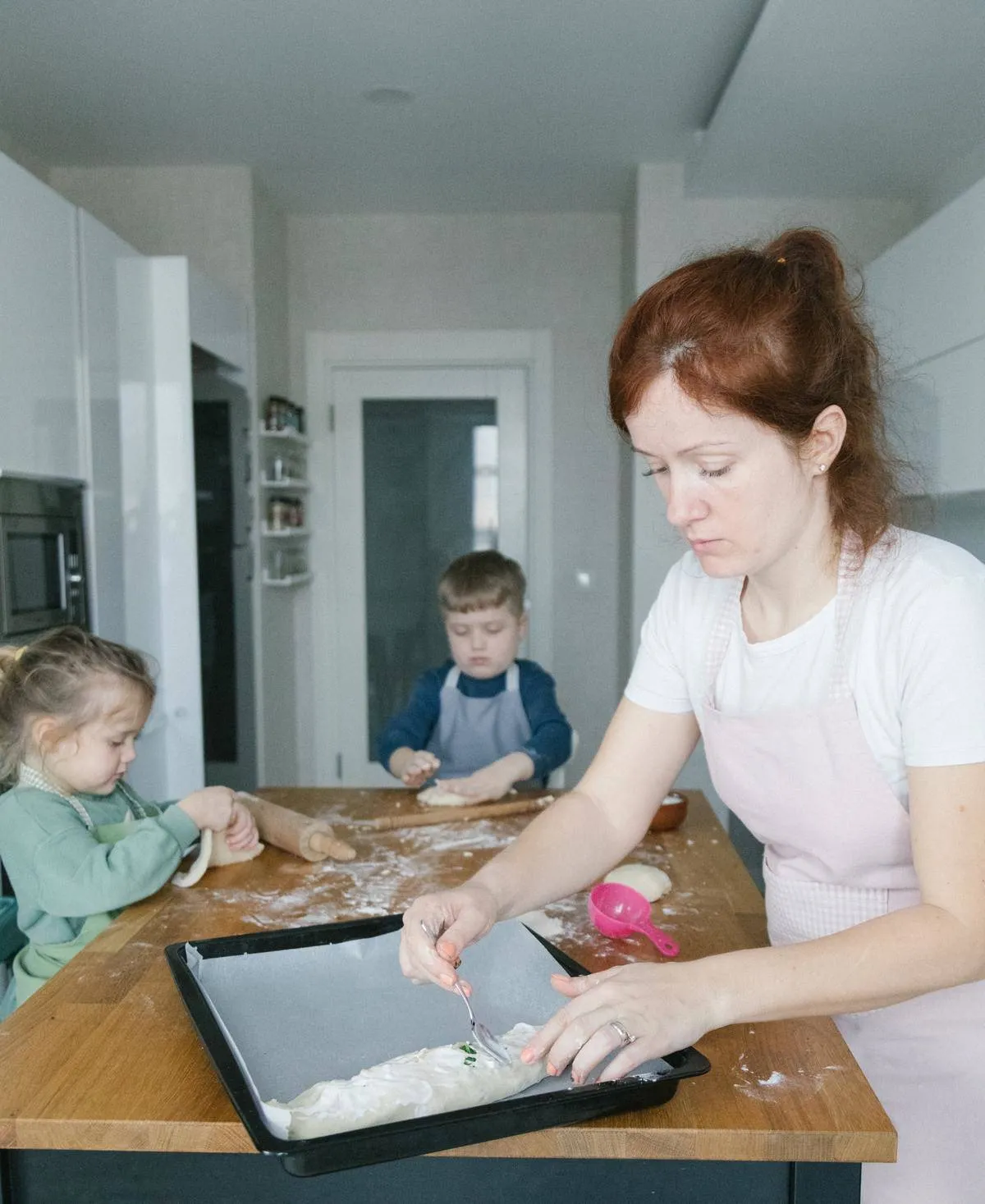 Young family in kitchen, mom baking, two kids helping