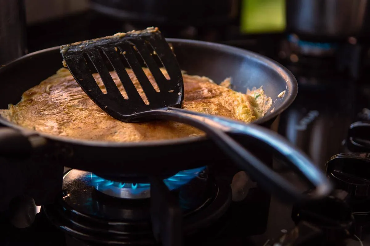 Omelet cooking on gas stove with a black spatula resting on top.