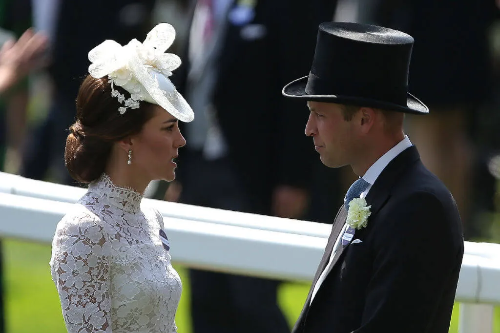 Duke and Duchess of Cambridge speak to one another at a formal event wearing top hat and floral head piece