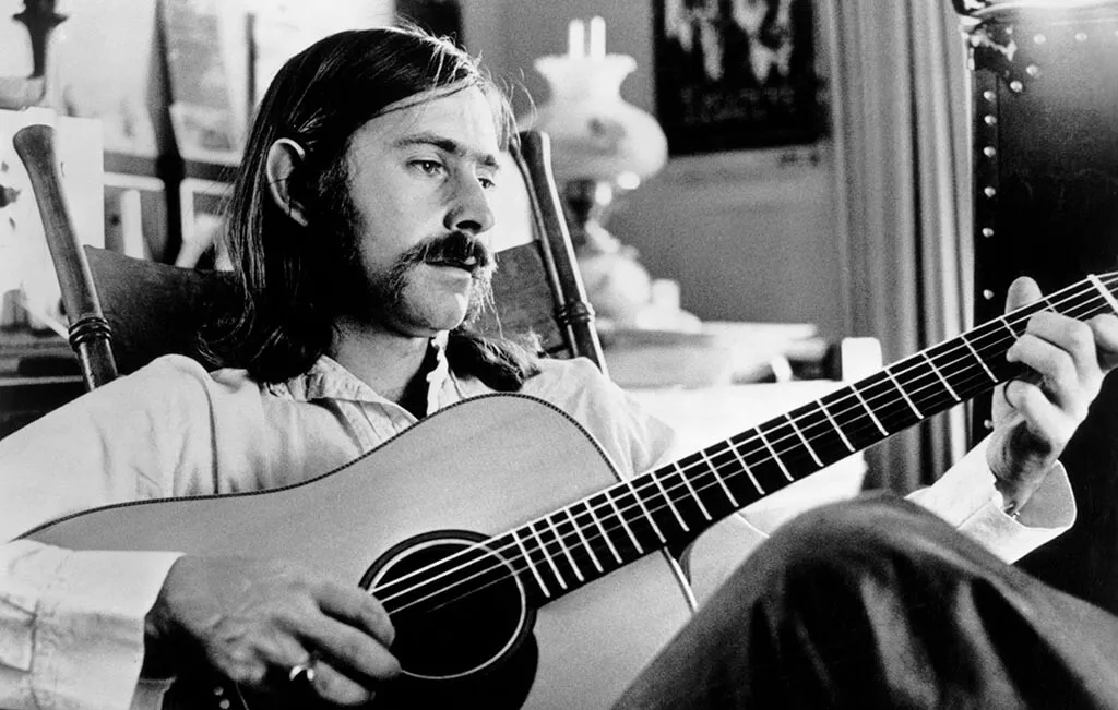 Norman Greenbaum holds acoustic guitar in black and white image 