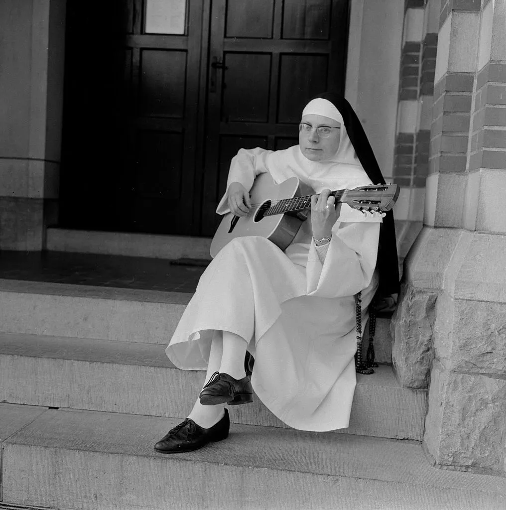 The Singing Nun, born Jeanne-Paule Marie Deckers, she is a nun at the Dominican Fichermont Convent in Fichermont, Belgium holds an acoustic guitar while seated on church steps