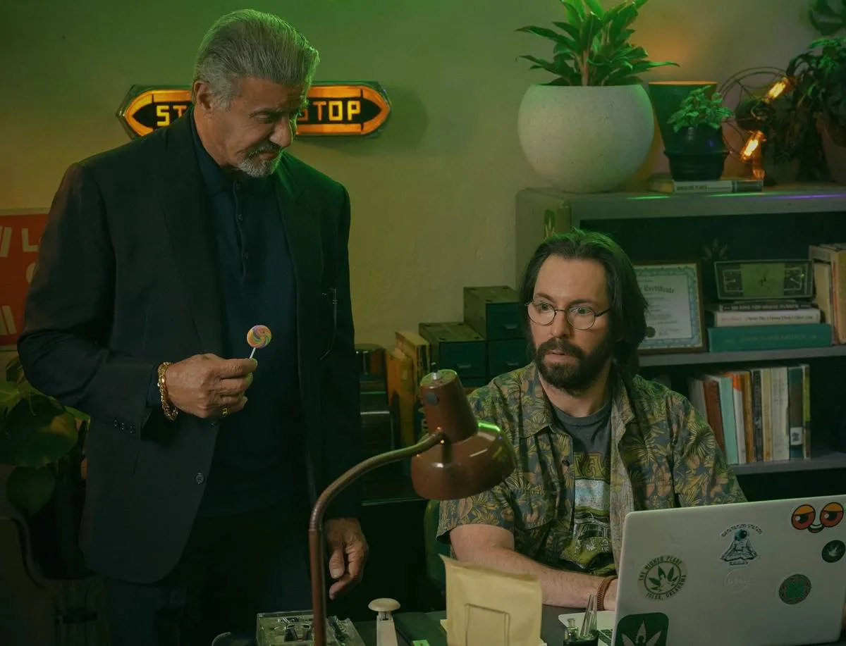 Sylvester Stallone as Dwight Manfredi standing over Martin Starr as Bodhi while he works on laptop in Tulsa King