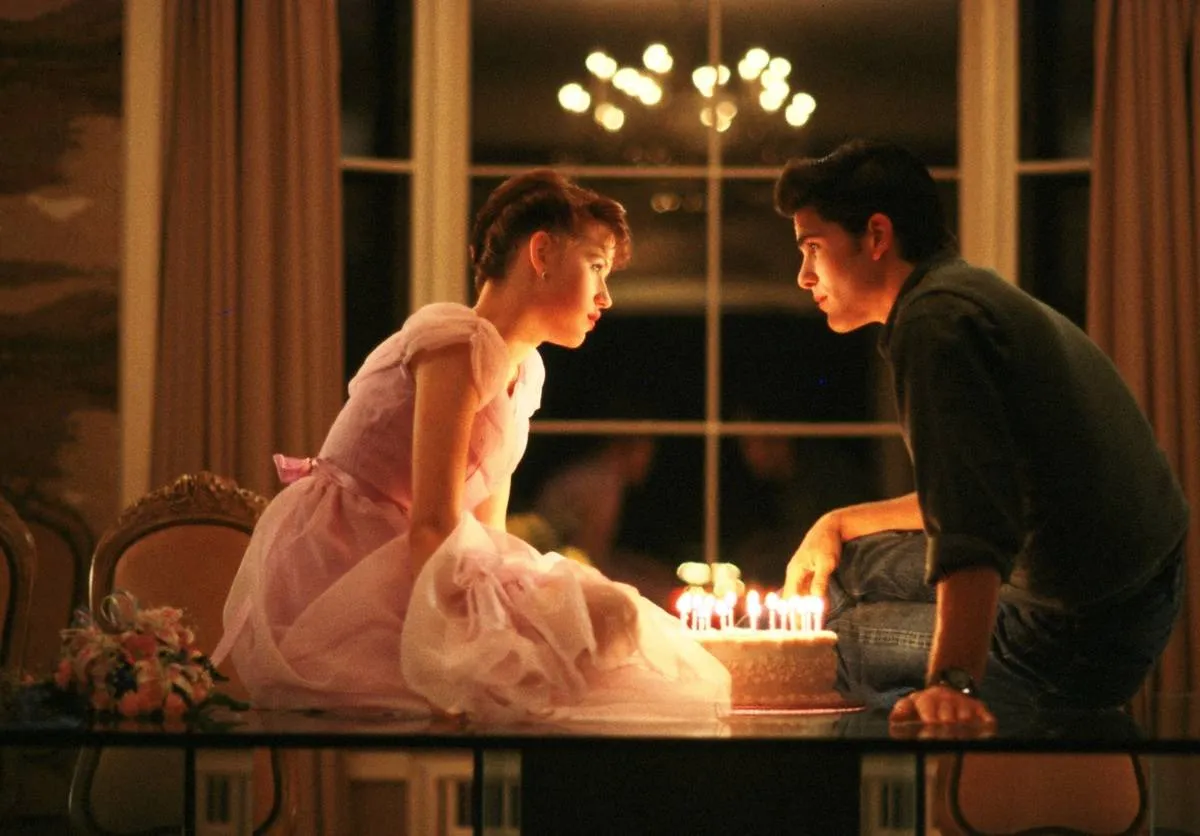 two teens sitting on a table with a birthday cake