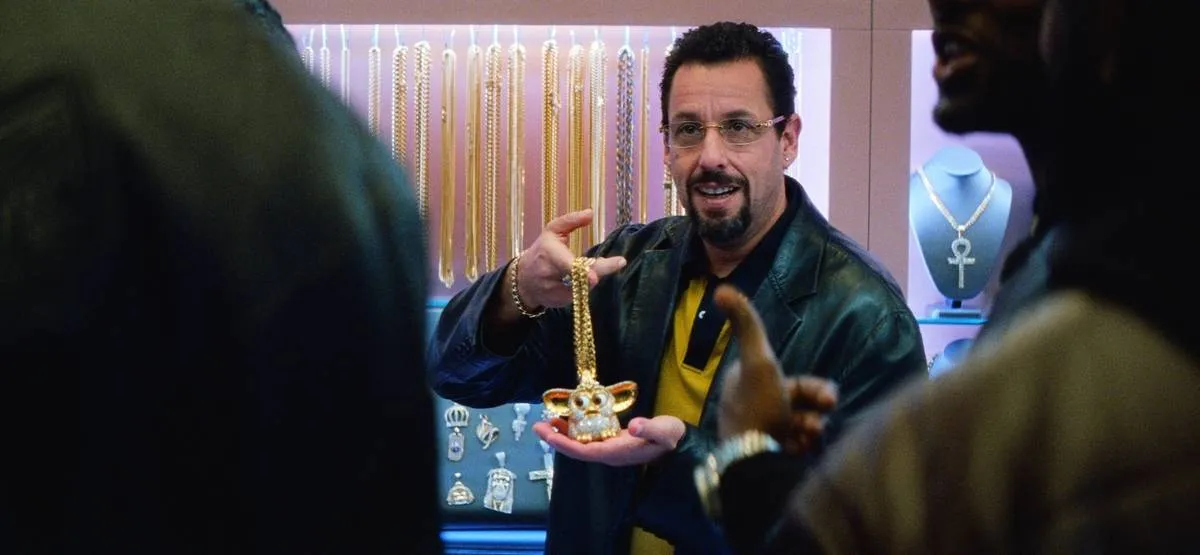 adam sandler holding a gold ferbie necklace in uncut gems